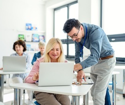 A man assists an older woman with her laptop