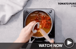 a wooden spoon stirs a soup as it simmers