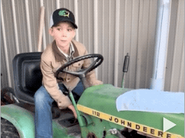 A boy sits on a tractor and smiles at the camera