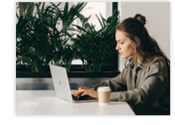 A young woman types on her laptop next to a cup of coffee