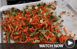 A fork stirs a baking sheet full of roasted vegetables